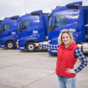 Female trucker standing in front of parked trucks and pointing her finger to the transportation vehicles.